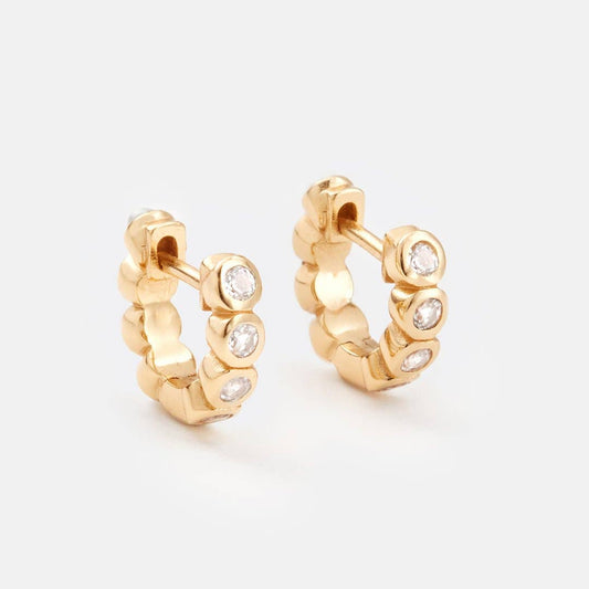 Gold hoop earrings with embedded diamonds on a light gray background