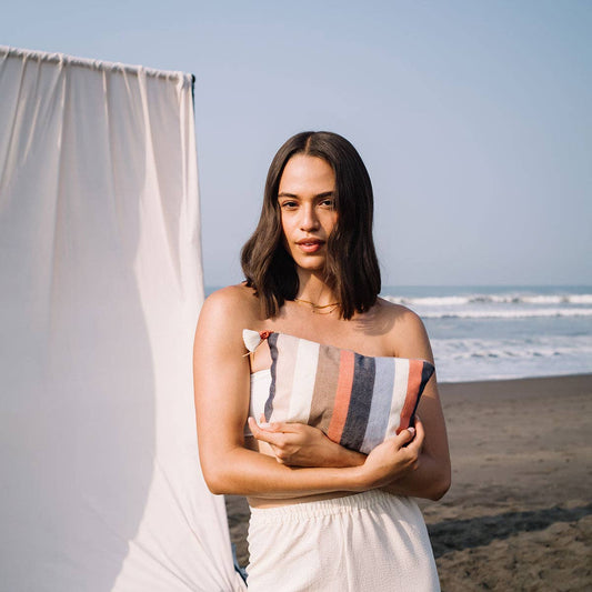 Woman holding a striped clutch on a beach with ocean and sky in the background