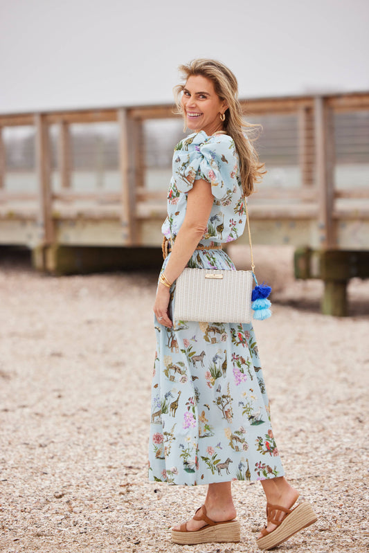 Woman in a floral dress standing on a pebbly beach with a wooden walkway in the background.