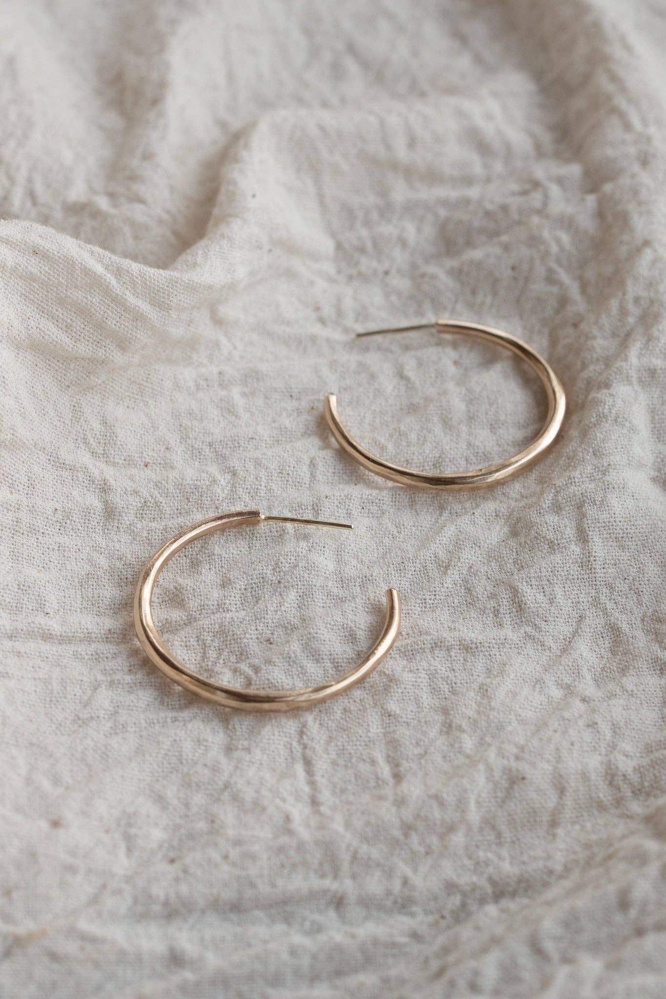 Gold hoop earrings on a textured beige fabric background