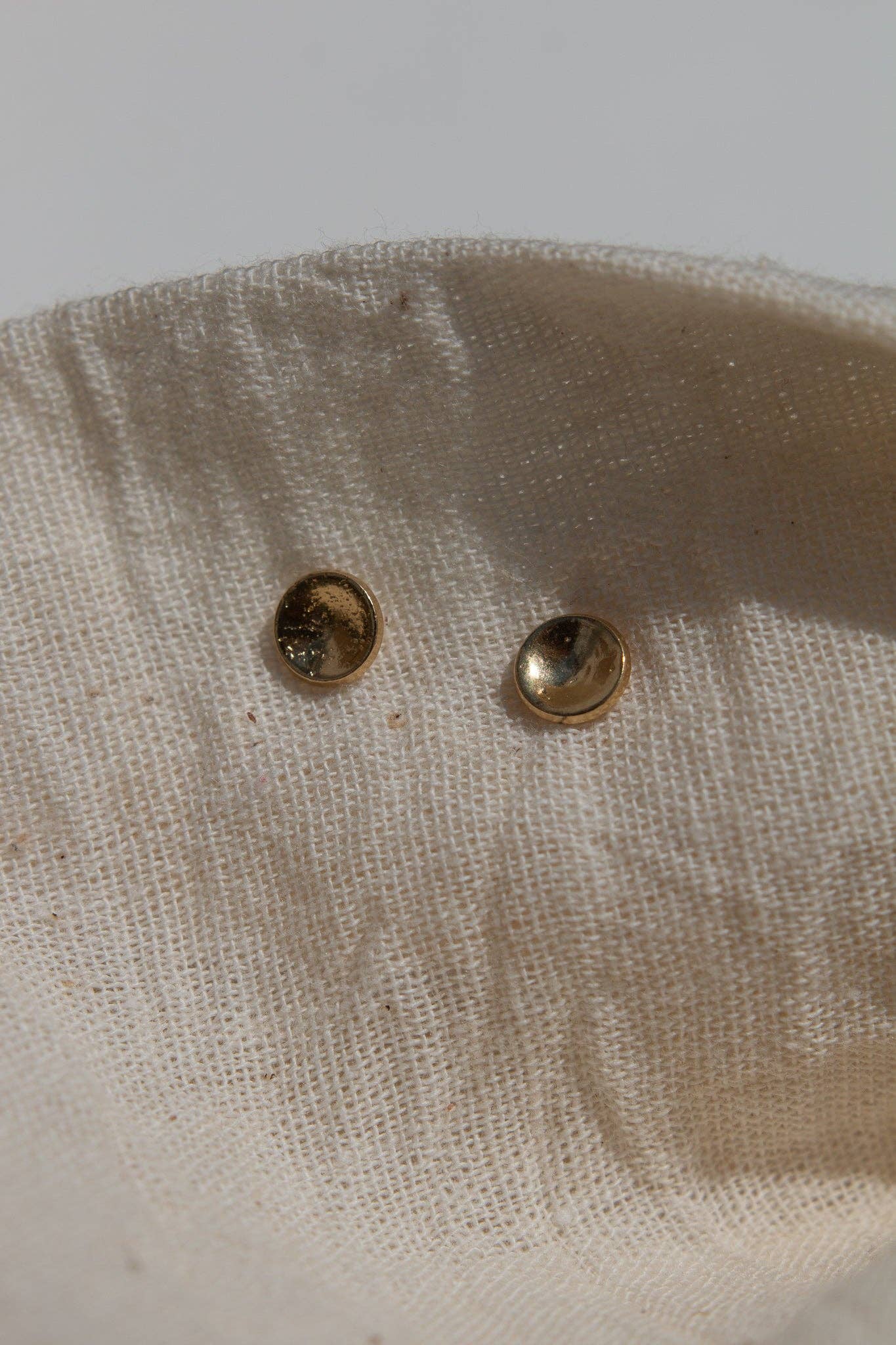 Two gold studs on a beige fabric background