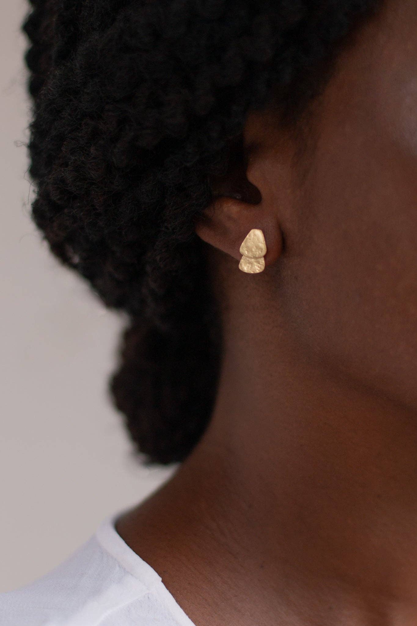 Close-up of a person wearing a gold earring with a neutral background