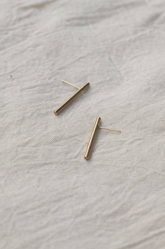 Gold bar earrings on a textured beige fabric background