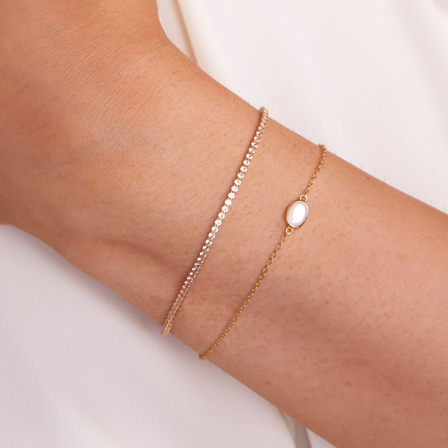 Gold bracelet with a central gemstone on a wrist against a light background