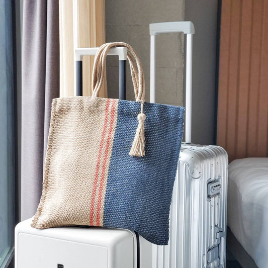 Woven tote bag with blue and orange stripes on a white suitcase in a room setting.