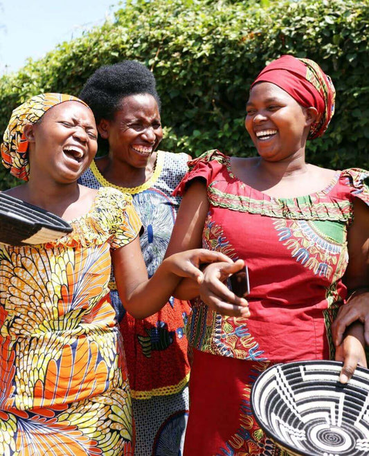 Three women in colorful traditional attire laughing outdoors.