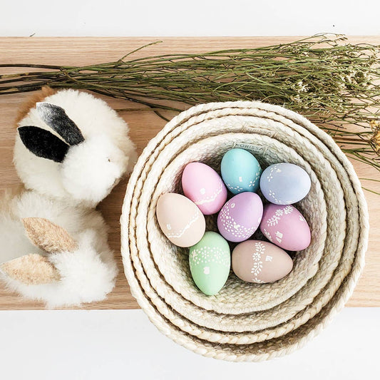 Pastel Easter eggs in a woven basket with a fluffy bunny toy on a wooden surface.