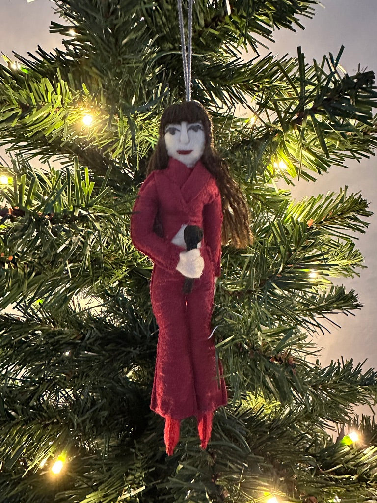 Ornament of a person in a red outfit hanging on a Christmas tree.