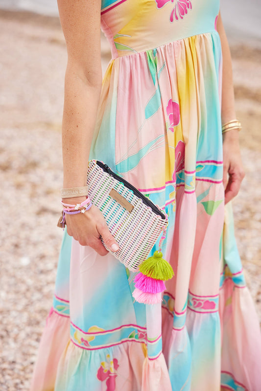Woman in a colorful dress holding a beaded clutch with tassels on a beach.