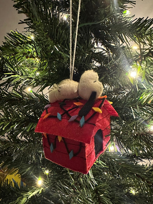 Decorative Christmas ornament with a red house and small figure on a lit Christmas tree.