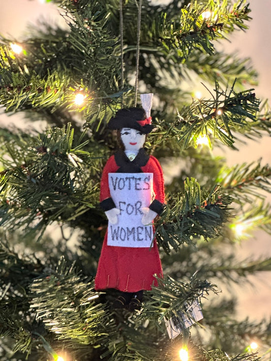 Suffragate ornament wearing a red and black coat and holding a "Votes for Women" sign hanging on a Christmas tree.