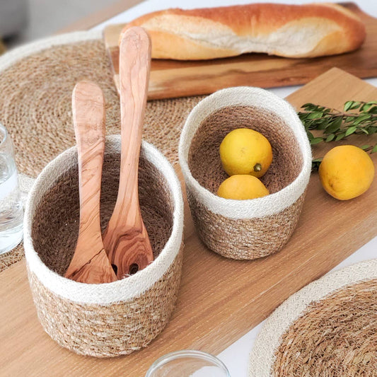 Two woven baskets with wooden spoons and lemons on a wooden surface with bread in the background.