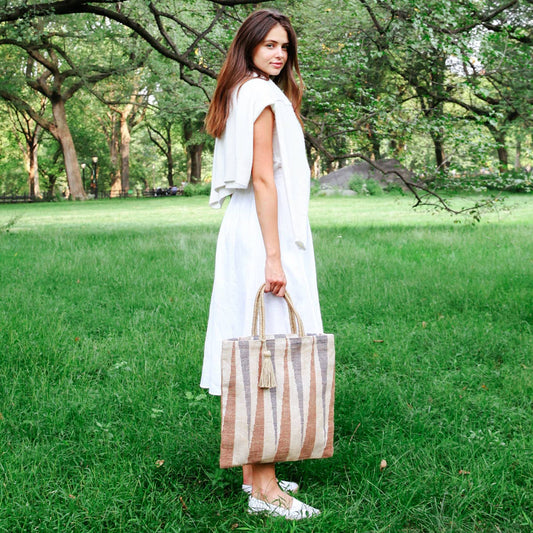 Woman in a white dress holding a striped bag in a park