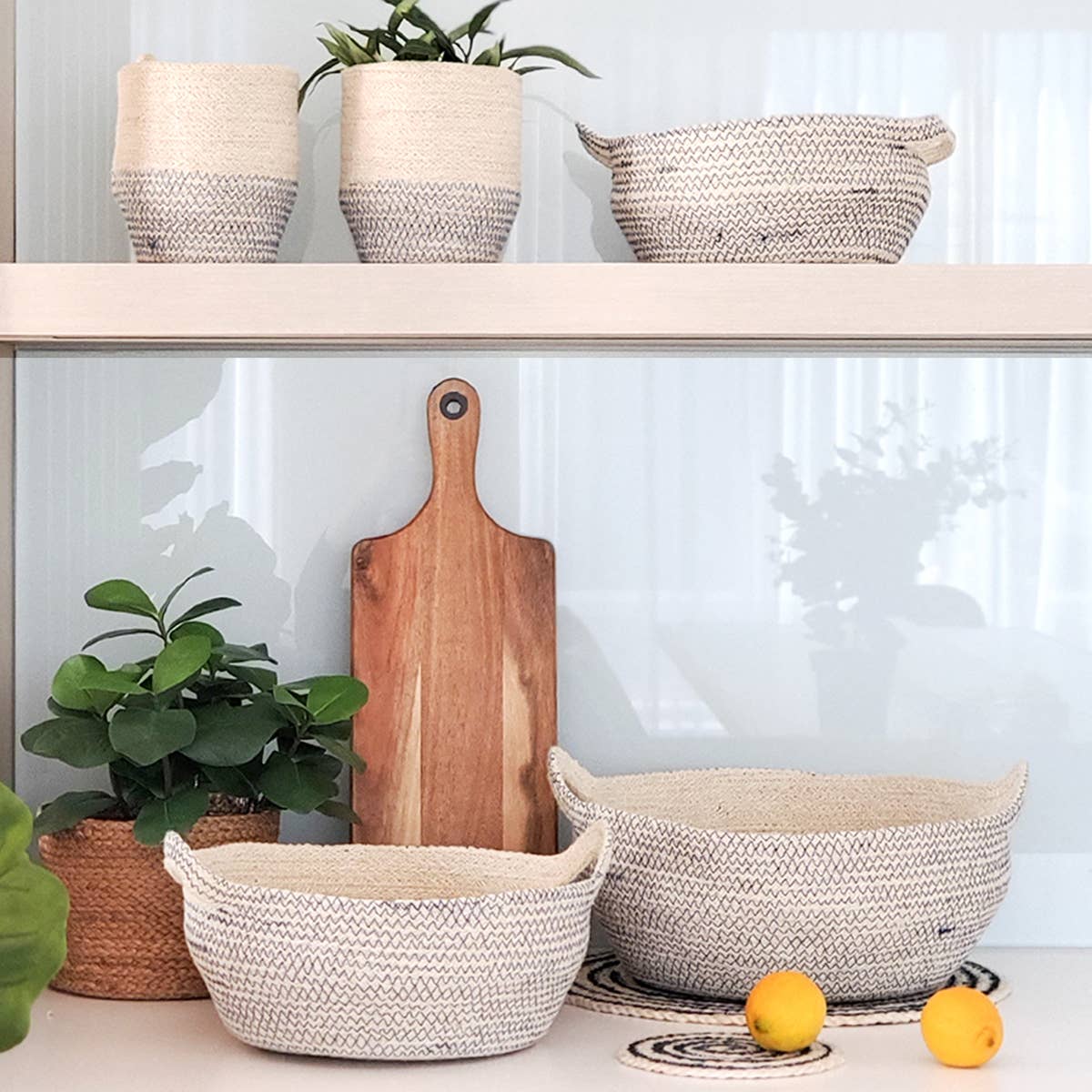 Woven baskets, a wooden cutting board, and potted plants on a shelf against a white wall.