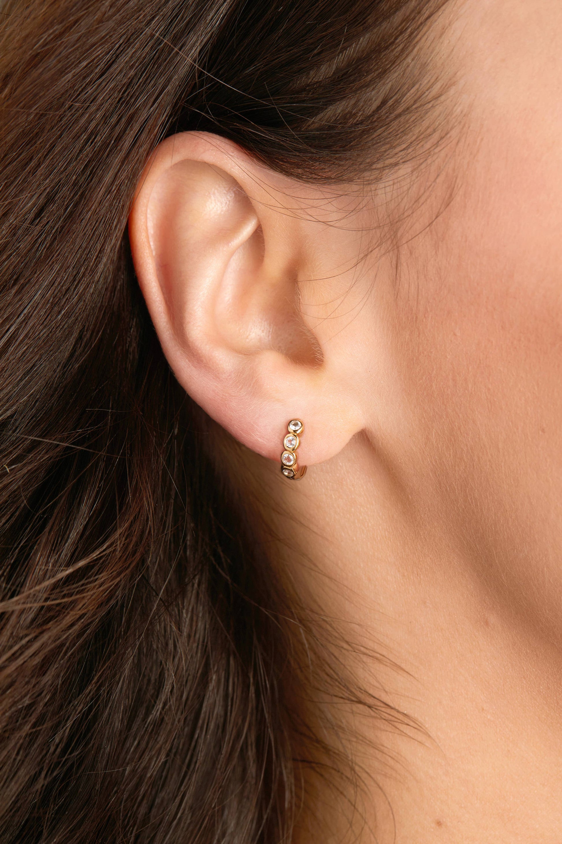 Close-up of an ear wearing a small gold earring with clear stones.