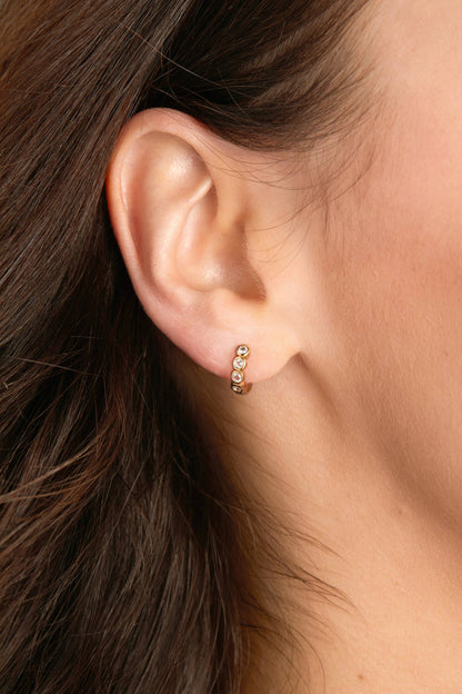 Close-up of an ear wearing a small gold earring with clear stones.