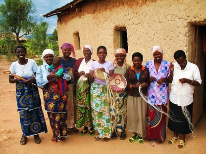 Group of women standing in front of a rustic building, holding handmade crafts.