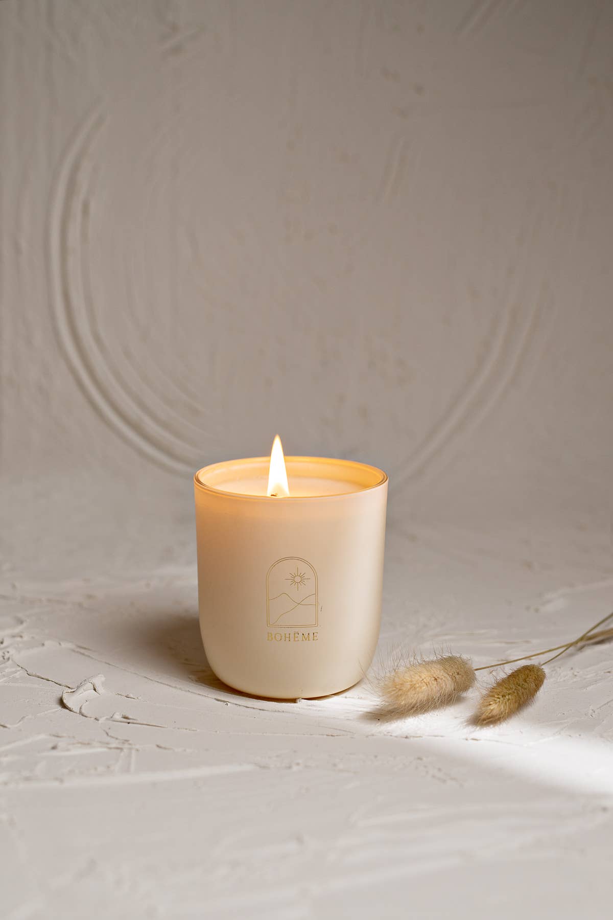 White candle with a flame on a textured beige surface