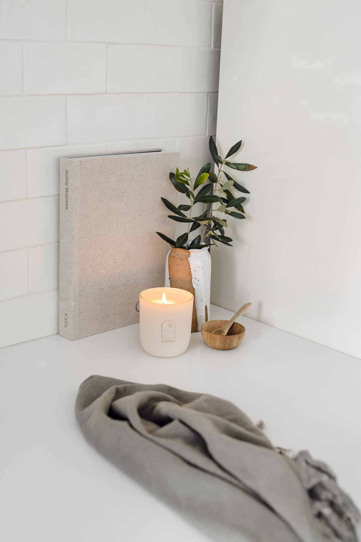 Candle, plant, and towel on a white surface with a white tiled wall in the background