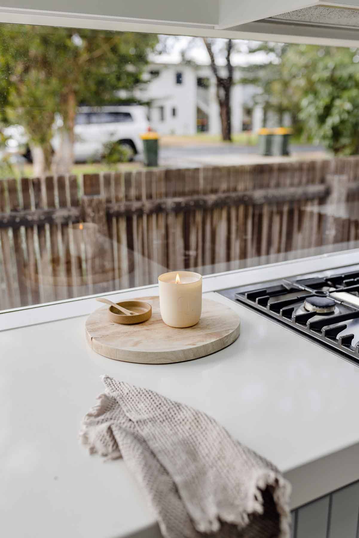 Candle on a wooden cutting board on a kitchen counter with a view of a canal.