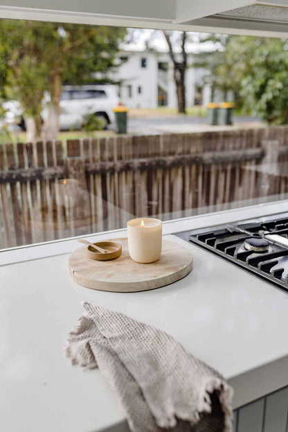 Candle on a wooden cutting board on a kitchen counter with a view of a canal.