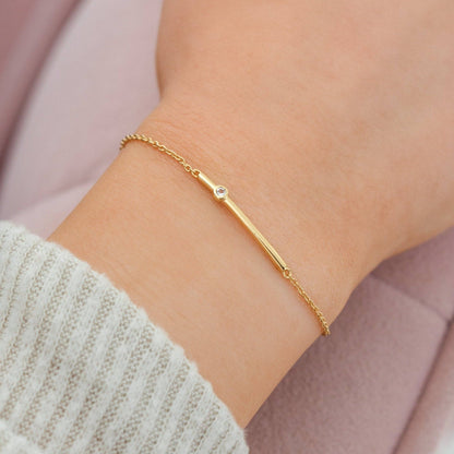 Gold bracelet with a small diamond on a wrist against a soft pink background