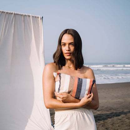 Woman holding a striped clutch on a beach with ocean and sky in the background