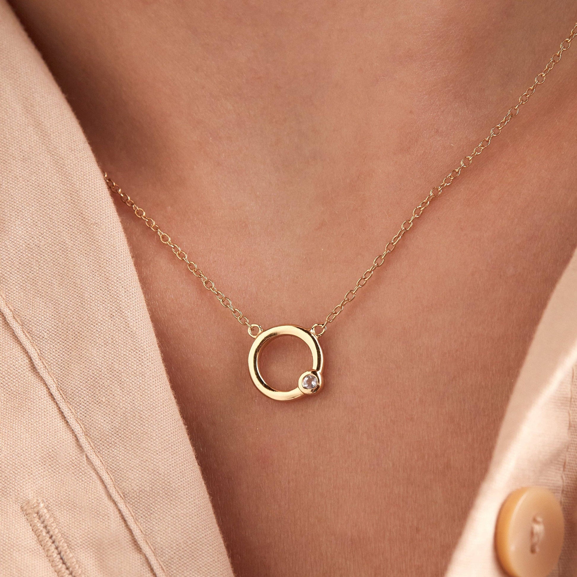 Gold necklace with a circular pendant on a person wearing a beige blazer.