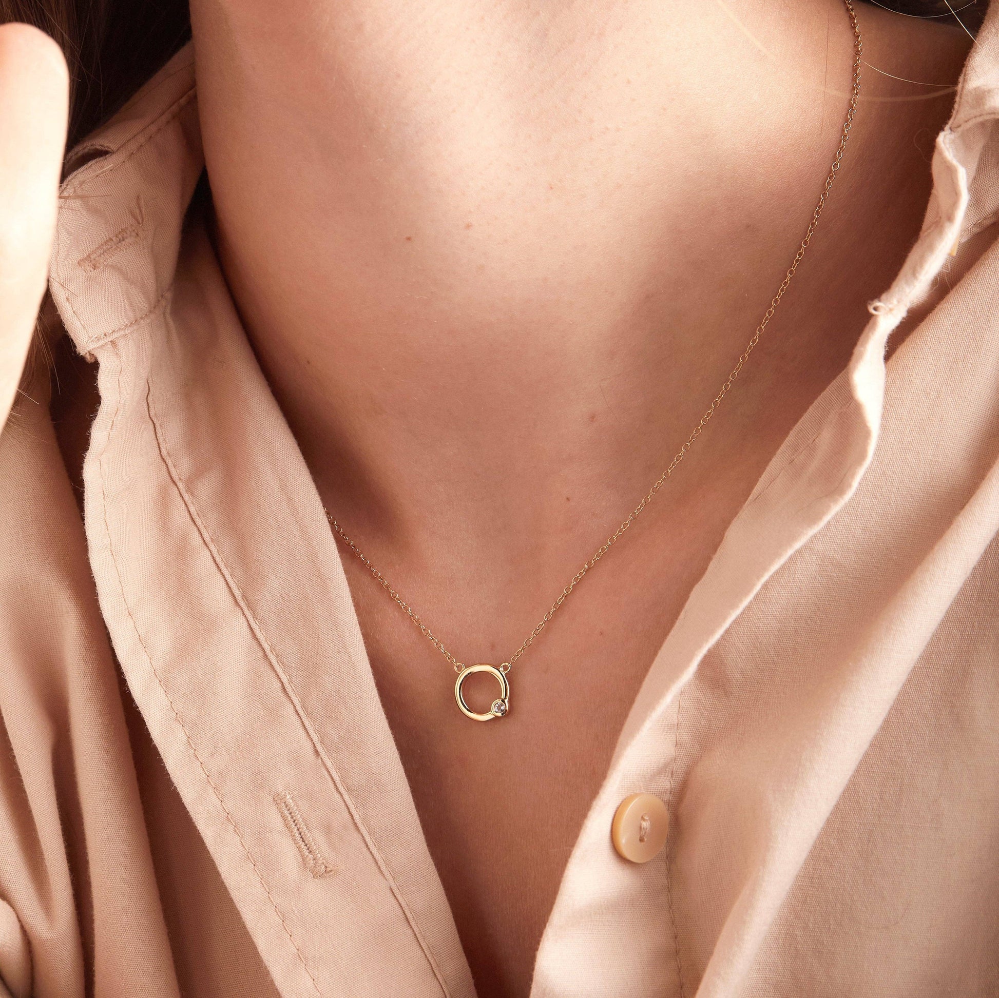 Gold necklace with a small pendant worn by a person in a pink shirt.