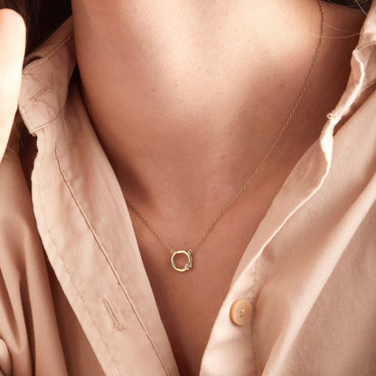Gold necklace with a small pendant worn by a person in a pink shirt.