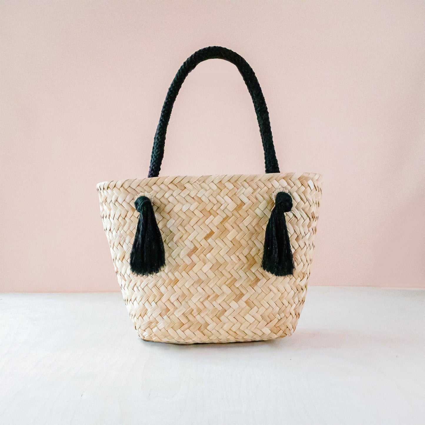 Woven handbag with black tassels on a light pink background