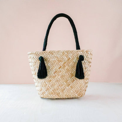 Woven handbag with black tassels on a light pink background
