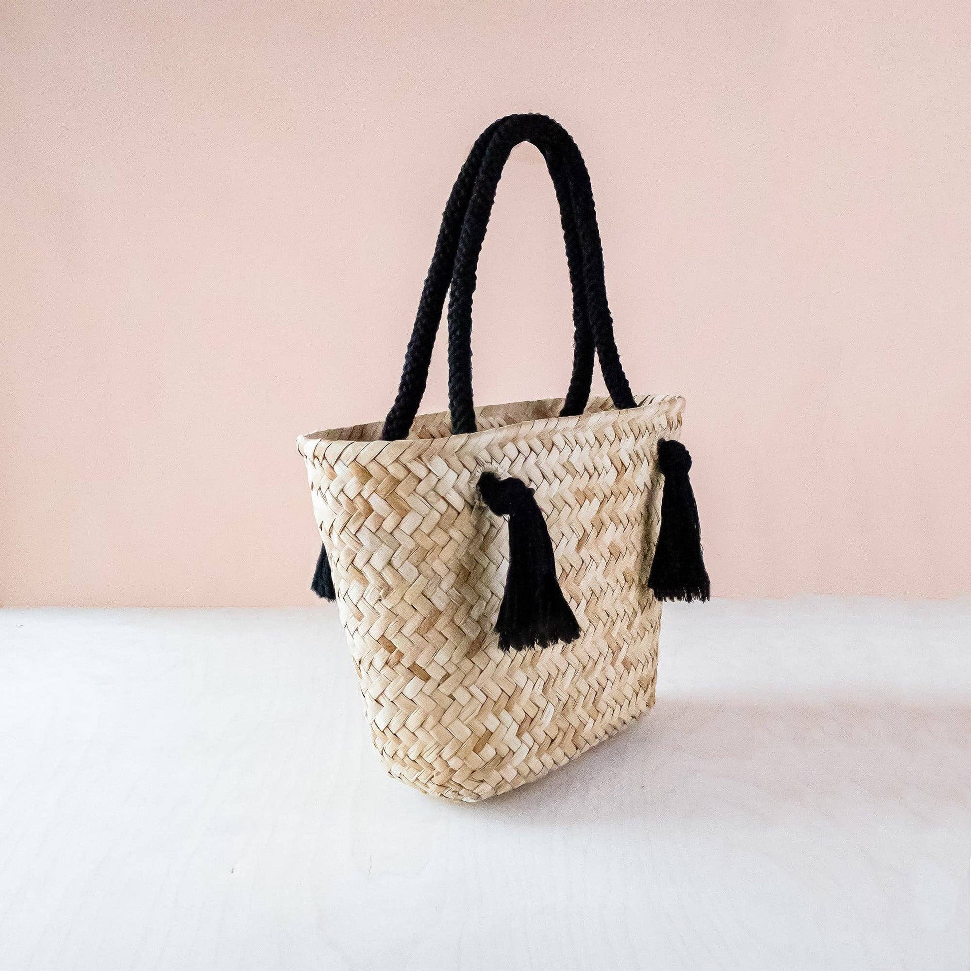 Woven handbag with black tassels on a light pink background