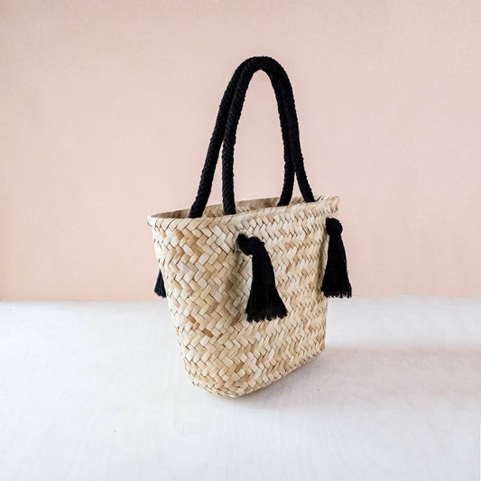 Woven handbag with black tassels on a light pink background