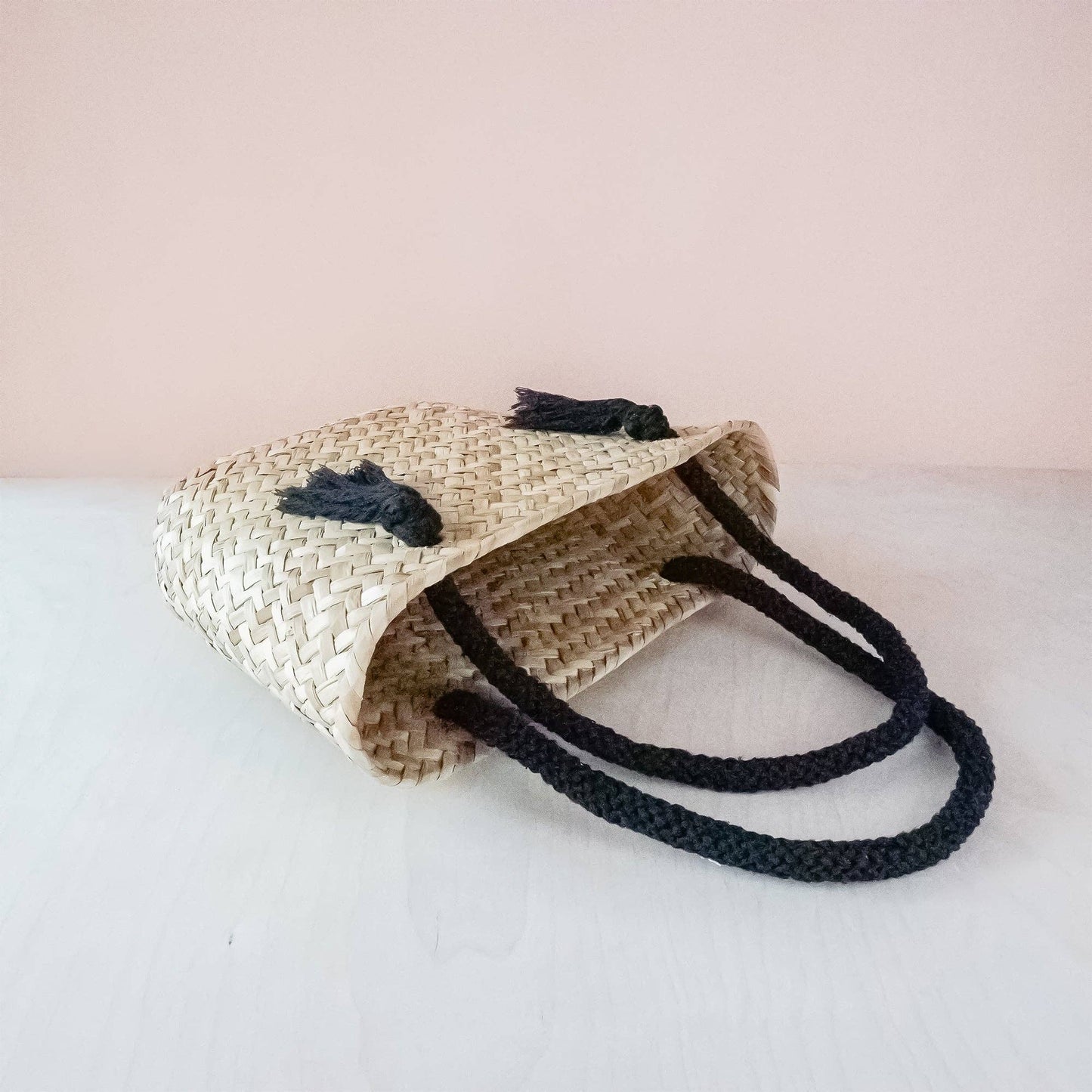 Woven bag with black handles on a light pink background