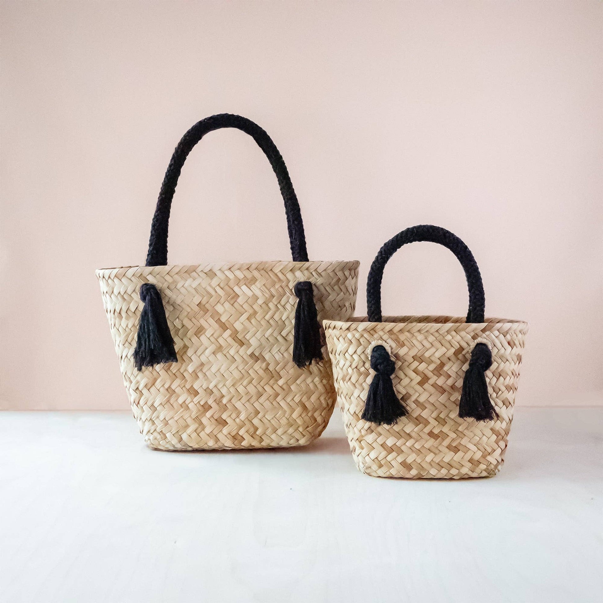 Two woven baskets with black tassels on a light pink background