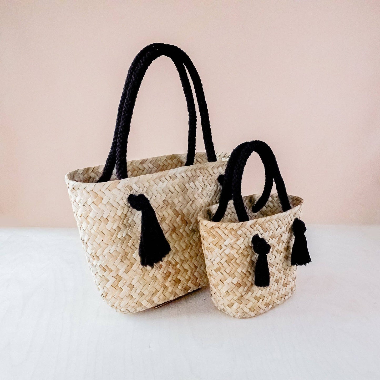 Two woven baskets with black handles and tassels on a light background