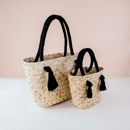 Two woven baskets with black handles and tassels on a light background