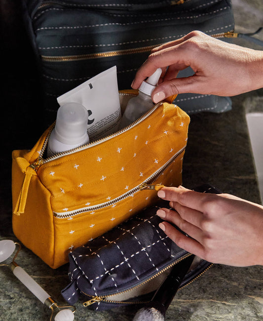 Person organizing items in a yellow makeup bag with a navy quilted bag underneath.