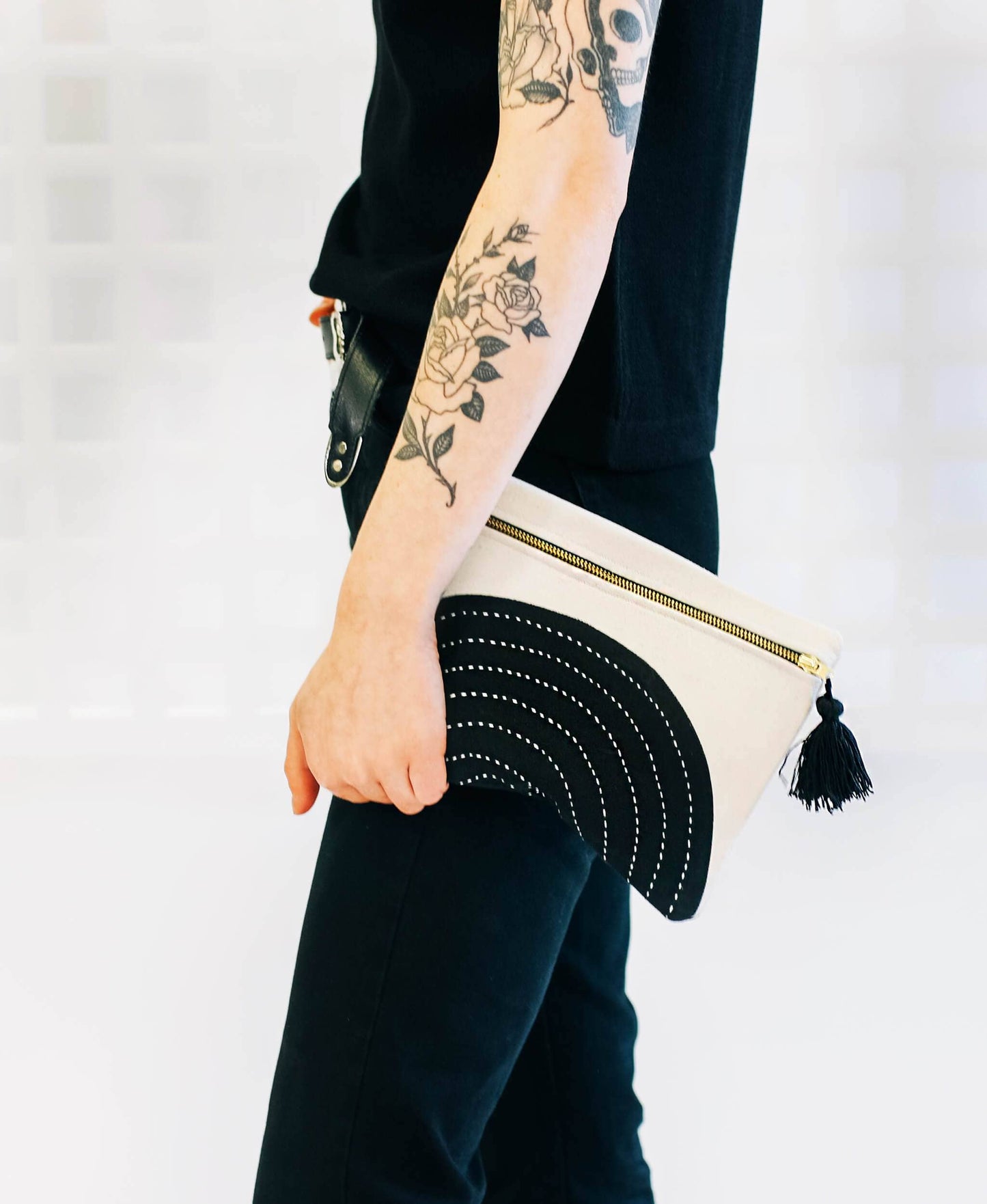 Person holding a white clutch with black accents and a tassel against a light background