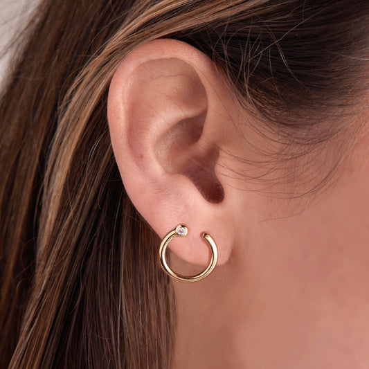Close-up of an ear wearing a gold hoop earring with a clear gemstone.