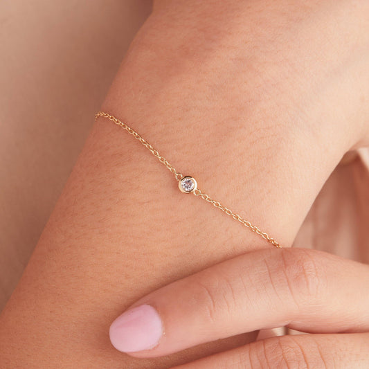 Rose gold bracelet with a small diamond on a wrist against a beige background