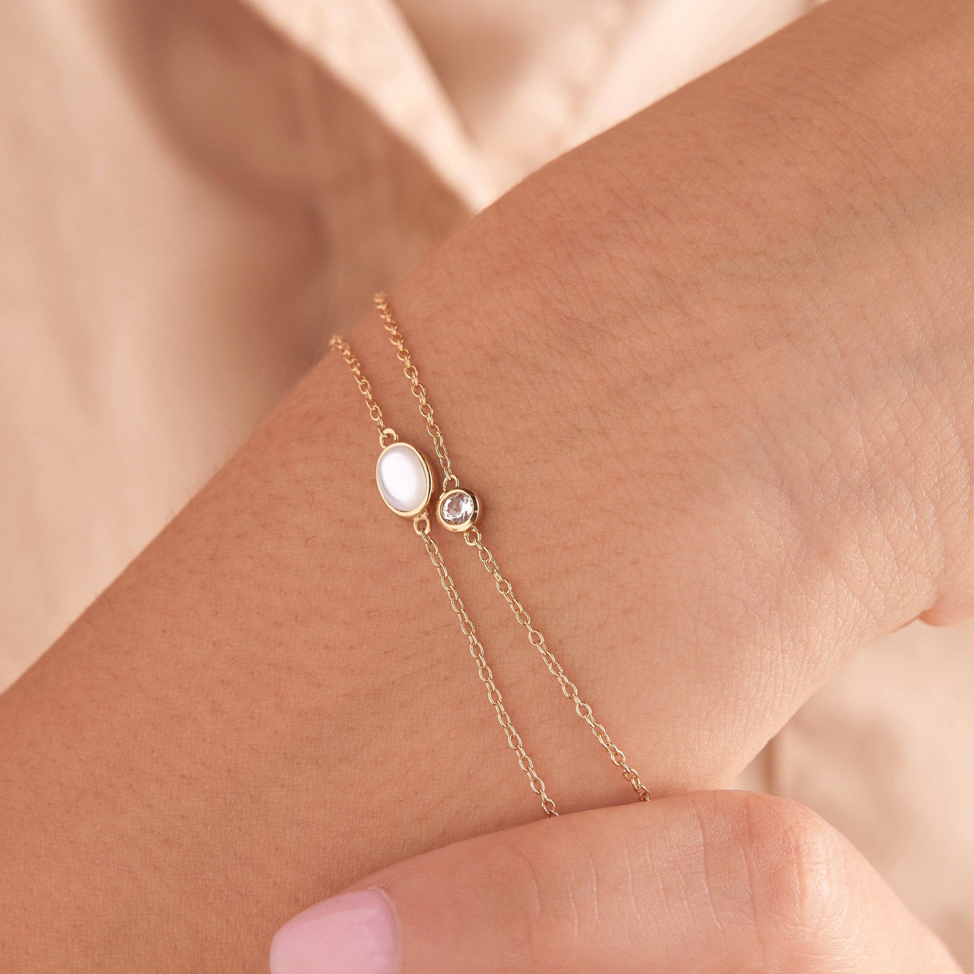 Gold bracelet with a central gemstone on a wrist against a beige background