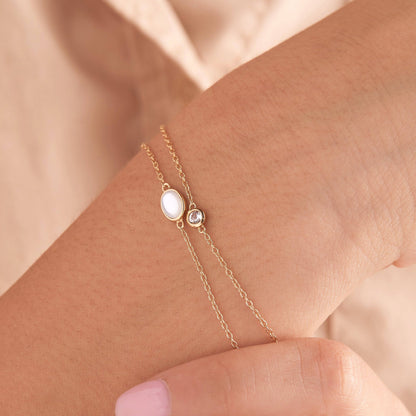 Gold bracelet with a central gemstone on a wrist against a beige background