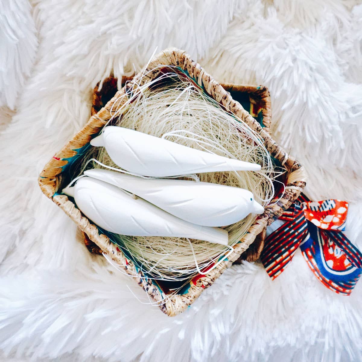 Decorative basket with white feathers and a colorful ribbon on a fluffy white surface