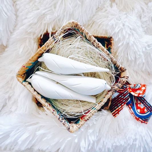 Decorative basket with white feathers and a colorful ribbon on a fluffy white surface