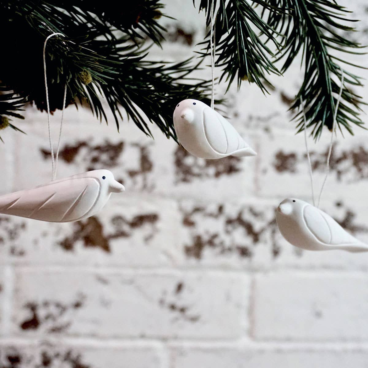 White ceramic birds hanging from a branch against a blurred background