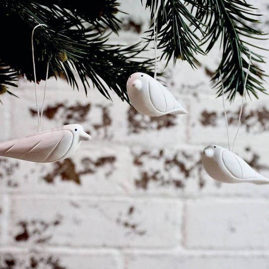 White ceramic birds hanging from a branch against a blurred background