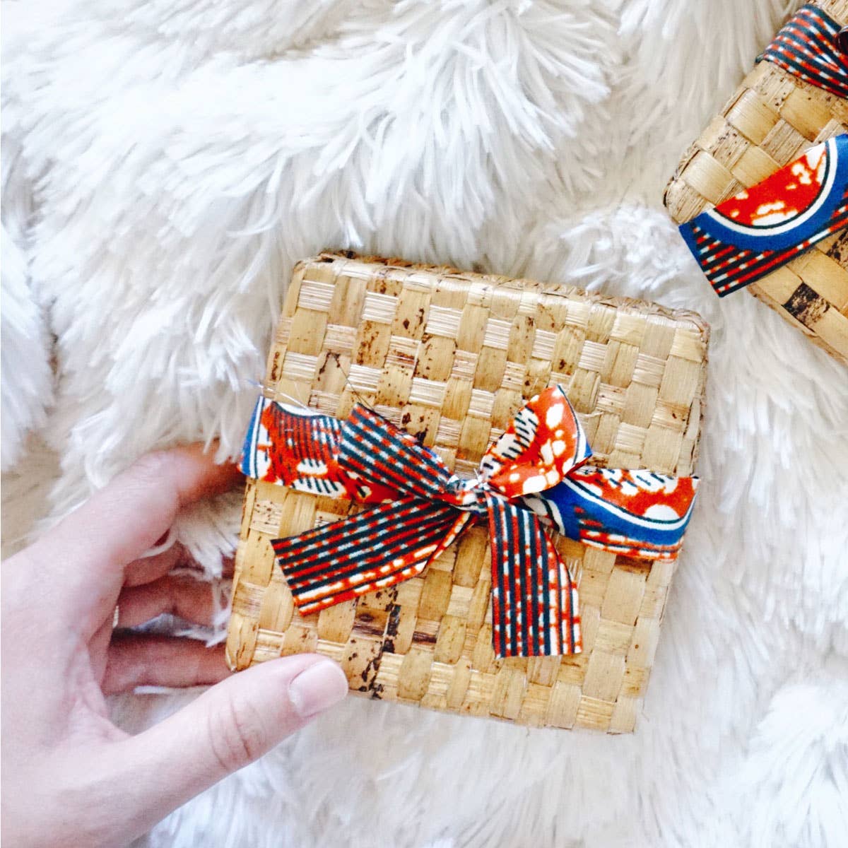 Woven pouch with decorative ribbons held by a hand on a fluffy white surface