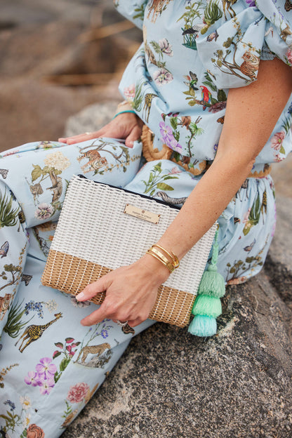 Person holding a woven clutch with tassel details, wearing a floral dress.